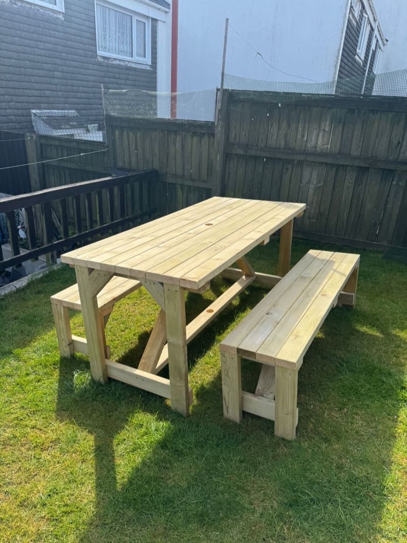 A handmade timber bench and table set standing on a lawn in a Cornish garden